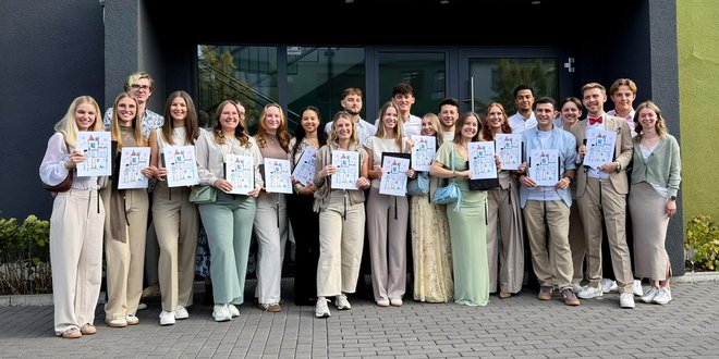 Physiotherapieschule Rhein-Nahe verabschiedet Kurs Ph24 Absolventinnen und Absolventen des Kurses Ph24 der Physiotherapieschule Rhein-Nahe stehen vor dem Gebäude der Schule und halten Ihre Abschlussurkunden in die Kamera.